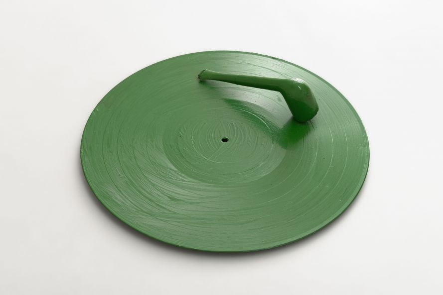 Multiple von Fluxus-Künstler Henning Christiansen: Eine Schallplatte, auf der eine Pfeife montiert ist. Das Objekt ist mit grüner Farbe überzogen.