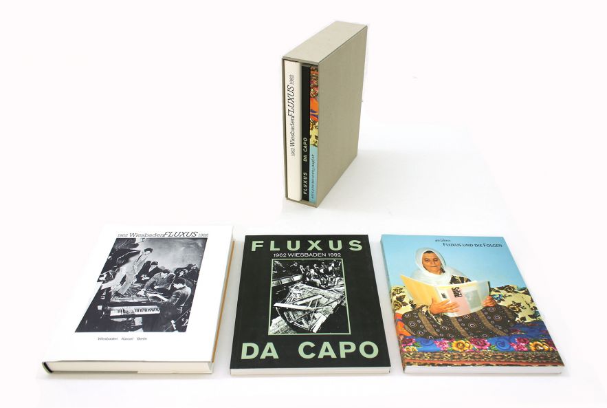 Drei Fluxus Kataloge liegen vor einem aufgestelltem Schuber aus grauem Karton