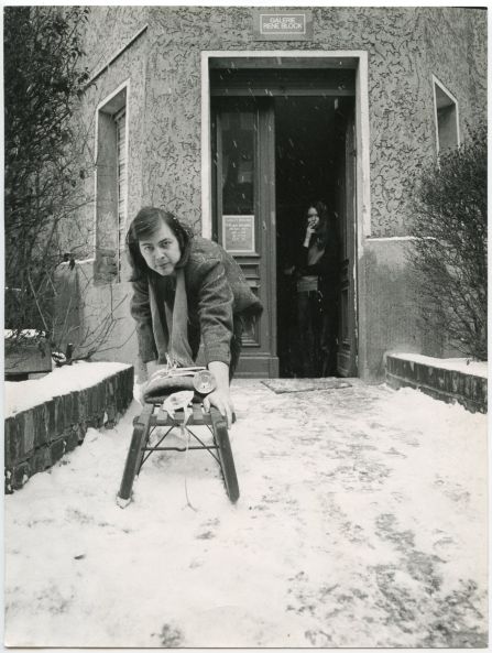 b/w photo showing a young René Block in the snow in front of the entrance to his gallery. He is leaning forward and pushing the Sledge by Joseph Beuys towards the camera.