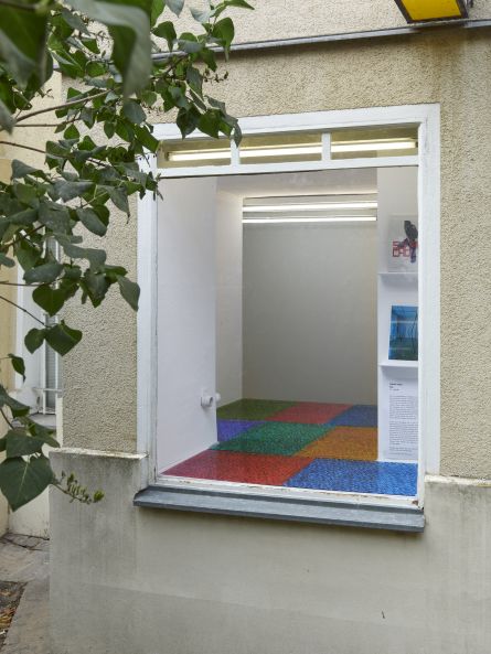 Blick auf ein Fenster. Im Innenraum hinter dem Fenster sind bunte Glasplatten ausgelegt