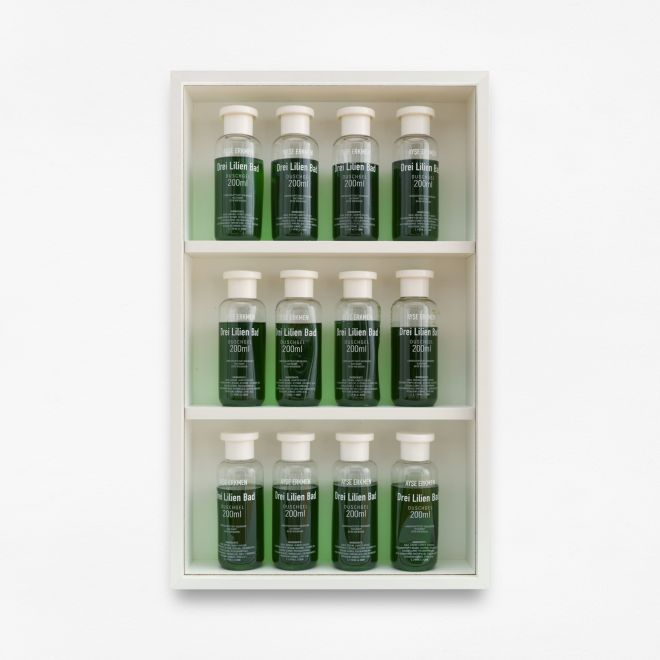 Edition von Ayse Erkmen. In einem weiß lackierten und verglasten Kasten sind auf drei Ebenen insgesamt zwölf Flaschen eines Duschgels in leuchtend grüner Farbe aufgereiht. Die Flaschen sind bedruckt mit: AYSE ERKMEN. Drei Lilien Bad. 200ml