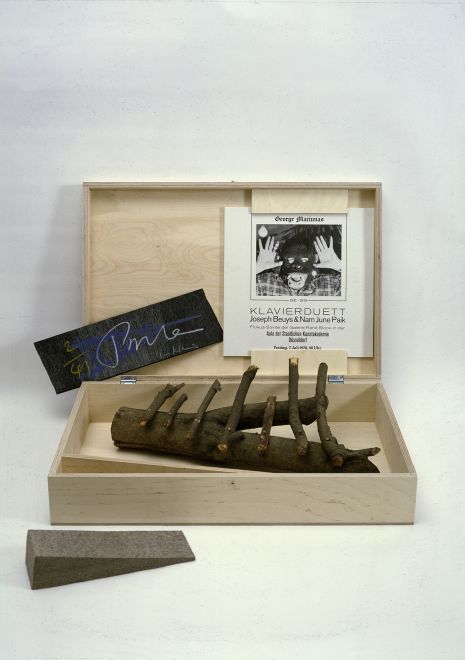 Edition von Joseph Beuys und Nam June Paik. Eine aufgeklappte Holzkiste mit dem Objekt Urklavier von Paik aus Ästen, einer in den Deckel der Kiste gespannten LP, einem schwarzen Karton mit der Nummerierung und der Signatur der Künstler und dem Filzkeil von Beuys.
