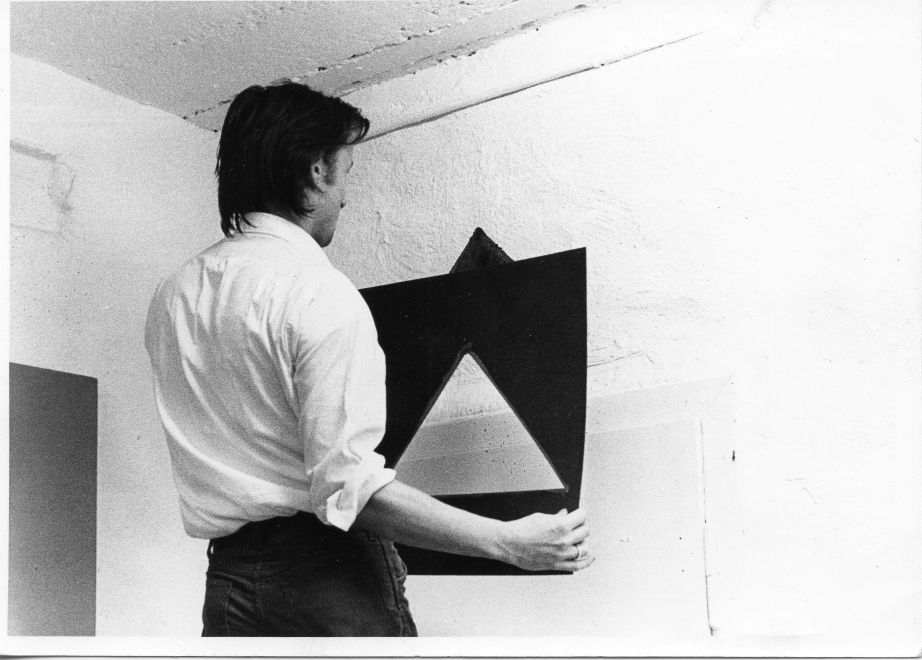 s/w Aufnahme zeigt Blinky Palermo als er gerade fertig ist, das blaue Dreieck mit der Schablone über einen Türrahmen zu malen