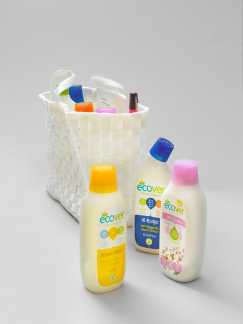 Edition von Maria Eichhorn. In einer weißen Tasche aus Bast stehen 4 verschiedene Reinigungsmittel mit bunten Kappen, und ein Faltblatt. Ein pinker Textmarker klemmt am Rand der Tasche. Vor der Tasche stehen drei zusätzliche Reinigungsmittel der Marke Ecover