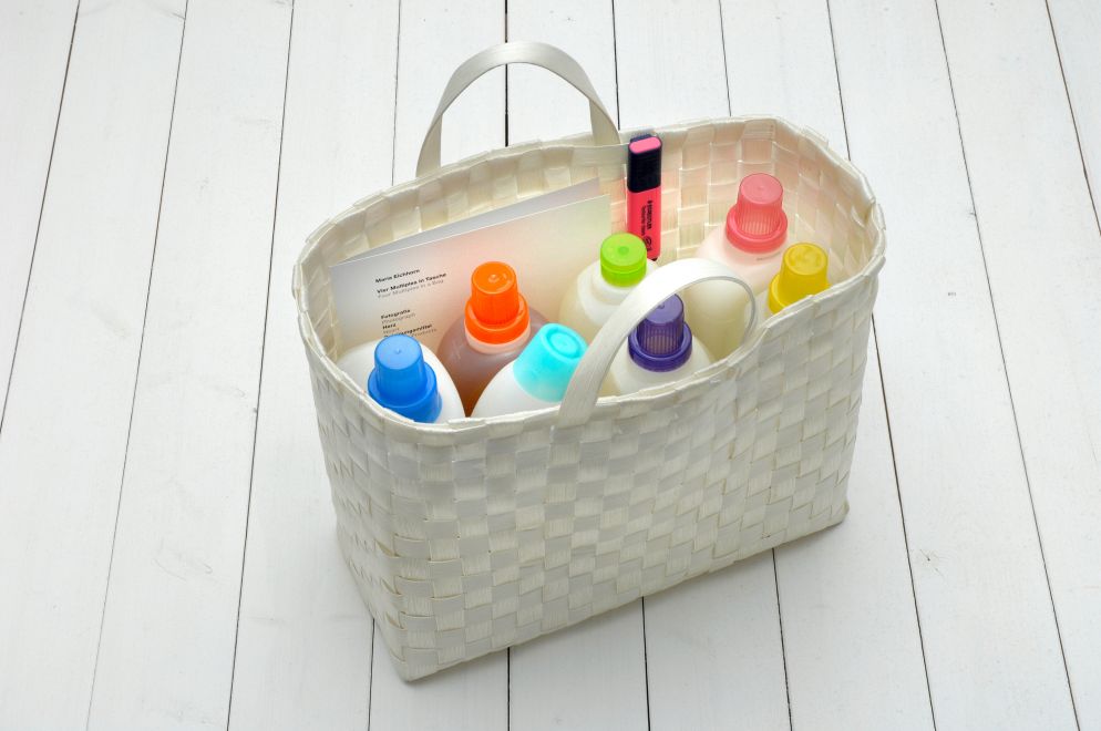 Edition von Maria Eichhorn. In einer weißen Tasche aus Bast stehen 7 verschiedene Reinigungsmittel mit bunten Kappen, und ein Faltblatt. Ein pinker Textmarker klemmt am Rand der Tasche.