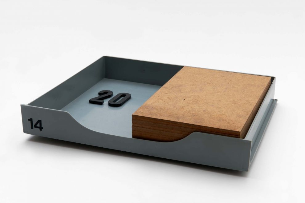 A gray plastic drawer with editions by Imi Giese and Imi Knoebel. The drawer contains a plastic number 20 and a stack of glued wood that fills half of the drawer.