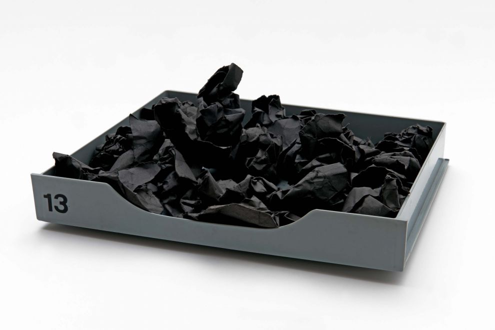 Multiple von Reiner Ruthenbeck. Eine graue Plastikschublade ist gefüllt mit Knäueln aus schwarzem Papier