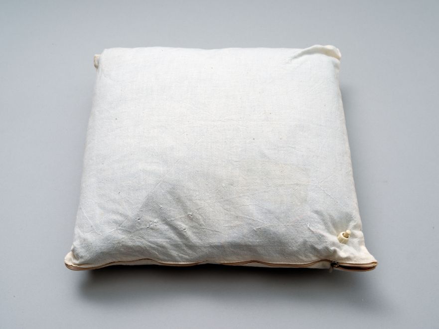 Edition von Hansjoachim Dietrich. Ein Kissen aus hellem Leinen mit einem eingenähten Schalter am rechten unteren Rand liegt auf grauem Hintergrund.
