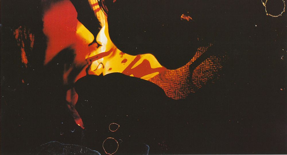 Abstract colored photo print by Rebecca Horn. Red and yellow amorphous shapes can be seen on a black surface, in which two kissing faces can be assumed.