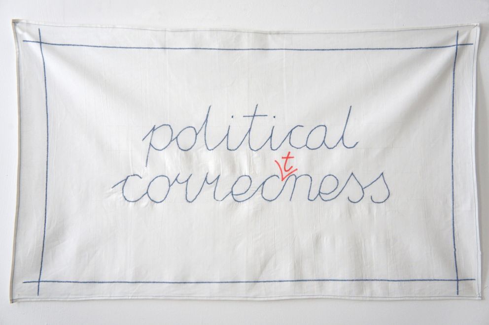 Edition von Jaroslaw Kozlowski. Ein Leinentuch mit Stickerei in handgeschriebener blauer Schrift mit Rechtschreibfehler: political correcness. Ein t ist mit rotem Edding hineinkorrigiert