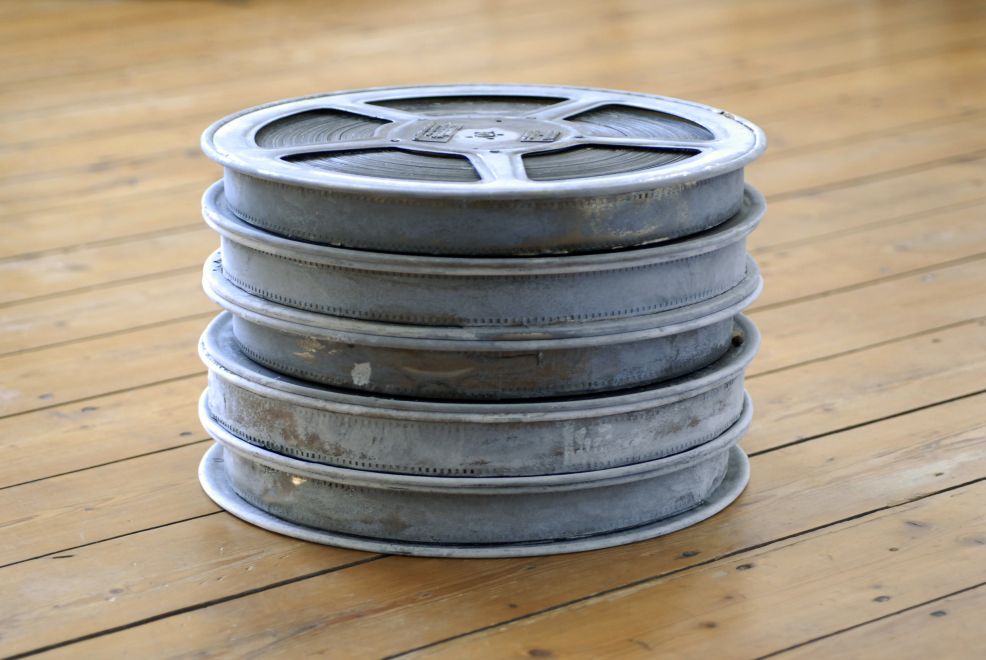 Edition des Künstlers Joseph Beuys. 5 galvanisierte Filmspulen des Films Das Schweigen von Ingmar Bergmann liegen übereinander auf einem Holzboden. Durch die dünne Zinkschicht ist die Oberfläche der Spulen in unterschiedlichen Grautönen, alle Details der Spulen sind aber noch zu erkennen.