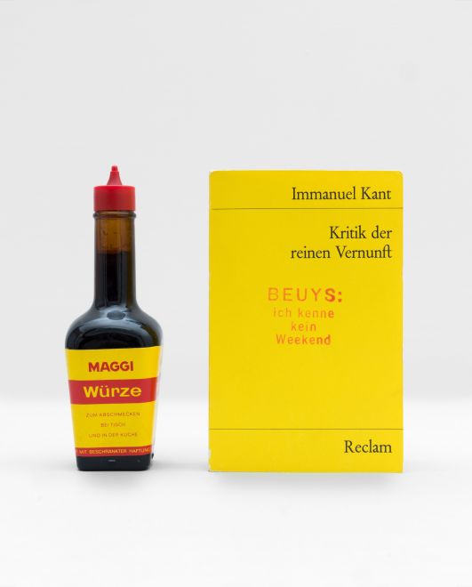 Multiple by the artist Joseph Beuys consisting of a bottle of Maggi staning next to the reclam book Immanuel Kant, Kritik der reinen Vernunft, that is stamped with BEUYS: ich kenne kein weekend in red ink.