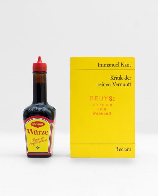 Multiple by the artist Joseph Beuys consisting of a bottle of Maggi staning next to the reclam book Immanuel Kant, Kritik der reinen Vernunft, that is stamped with BEUYS: ich kenne kein weekend in red ink.