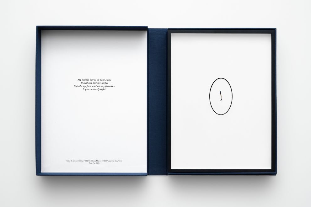 Edition der Künstlerin Alicja Kwade. Eine geöffnete Kassette aus dunkelblauem Leinen mit einem im Passepartout gerahmten abgebrannten Kerzendocht und einem Gedicht im Deckel.