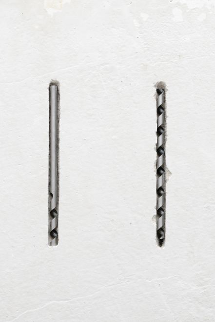 Edition von Christine Moldrickx. Ein Bohraufsatz ist in zwei Hälften geteilt, die parallel zueinander länglich in eine Wand eingelassen sind
