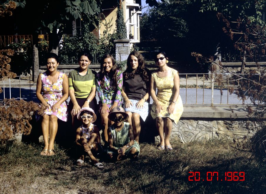 Offsetdruck von Aydan Murtezaoglu. Eine Familie bestehend aus 5 Frauen unterschiedlichen Alters und zwei Kindern sitzen in leichter Sommerkleidung vor einer Terrasse. Unten rechts steht in rot das Datum der Aufnahme: 20.07.1969