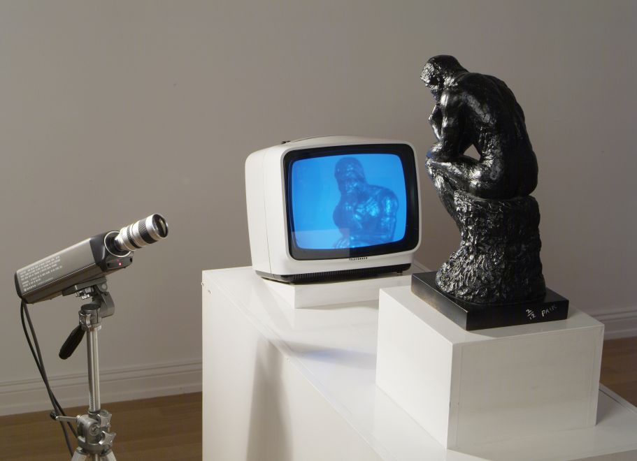 Video-Multiple von Nam June Paik: Closed-Circuit-Installation mit einer kleinen Rodin-Denker-Statuette, die sich auf einem Monitor betrachtet. Monitor und Figur sind auf einem weißem Sockel inszeniert.