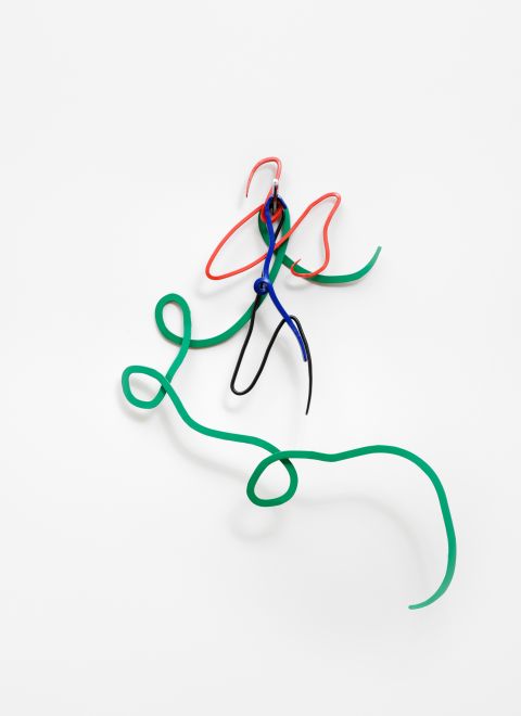 Edition von Navid Nuur. Geschwungene Metallformen in den Farben Grün, Rot, Blau und Schwarz hängen an einem silbernen Mehrfarbkugelschreiber an einer weißen Wand. Die Formen sehen aus wie bunte Kritzeleien