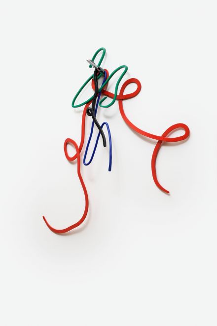 Edition von Navid Nuur. Geschwungene Metallformen in den Farben Grün, Rot, Blau und Schwarz hängen an einem silbernen Mehrfarbkugelschreiber an einer weißen Wand. Die Formen sehen aus wie bunte Kritzeleien