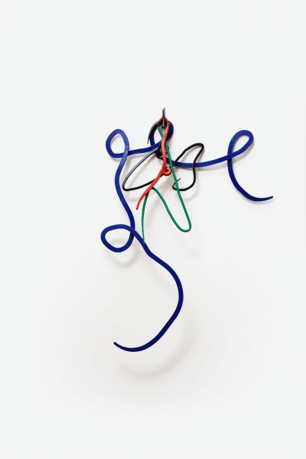 Edition von Navid Nuur. Geschwungene Metallformen in den Farben Grün, Rot, Blau und Schwarz hängen an einem silbernen Mehrfarbkugelschreiber an einer weißen Wand. Die Formen sehen aus wie bunte Kritzeleien