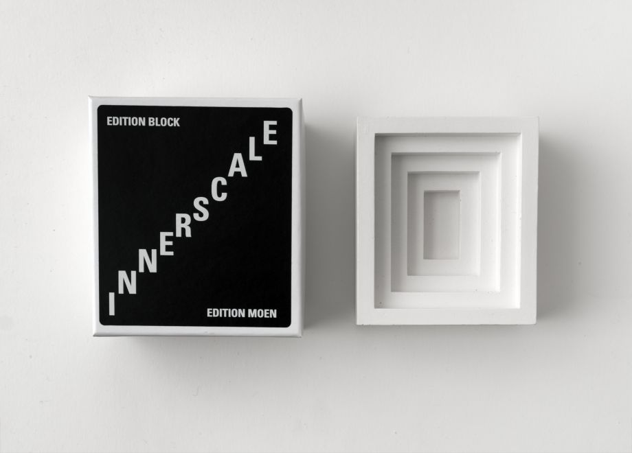 Multiple des Künstlers Bjørn Nørgaard. Gipsmodel einer konkav in fünf Stufen nach innen zulaufenden rechteckigen Form, eine Negativ-Form. Daneben liegt die passende Box aus Pappe. Darauf steht INNERSCALE, die Buchstaben sind so versetzt dass die selbst Stufen bilden
