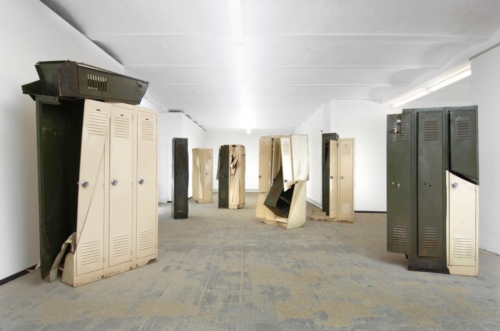 Edition by Olaf Metzel. A group of beige and olive-green metal lockers that have been destroyed with an angle grinder and reassembled. They are reminiscent of cubist compositions