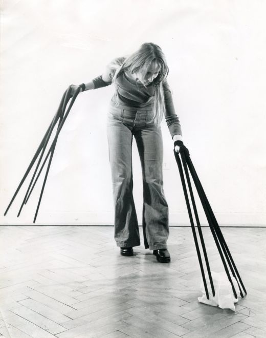 Schwarz-weiß Foto zeigt die Künstlerin Rebecca Horn, die mit den Handschuhfingern ein Tuch vom Boden aufhebt.