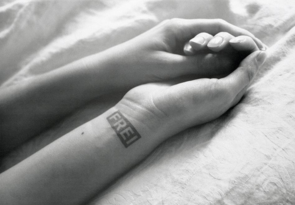 Offset print by Sejla Kameric, A black and white photo of the forearms and hands of a woman on a linen cloth. The hands are placed one inside the other. On the inside of the right wrist is a stamp that reads FREI