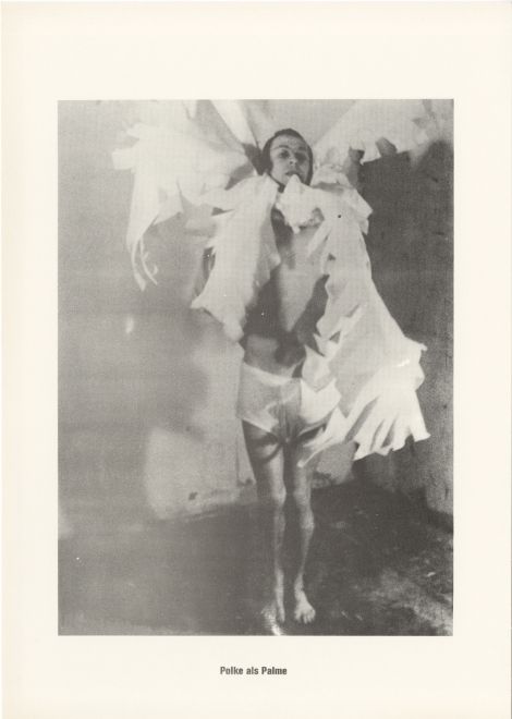 Druck von Sigmar Polke aus der Serie höhere Wesen befehlen. s/w Foto von Polke, um dessen Hals Palmwedel aus Papier befestigt sind. Darunter steht: Polke als Palme