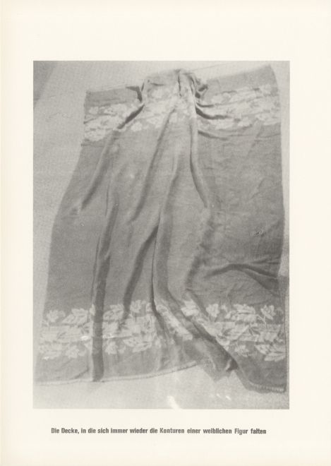 Druck von Sigmar Polke aus der Serie höhere Wesen befehlen. s/w Foto einer ausgebreiteten Decke mit Falten. Darunter steht: Die Decke, in die sich immer wieder die Konturen einer weiblichen Figur falten