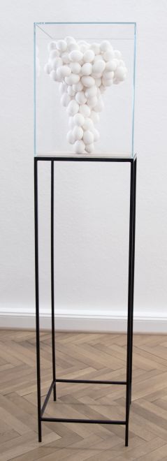 Edition von Mariana Vassileva. Ein aus weißen Eiern geformter Atompilz steht unter einer Haube aus Acrylglass auf einem hohen Gestell aus schwarzem Metall