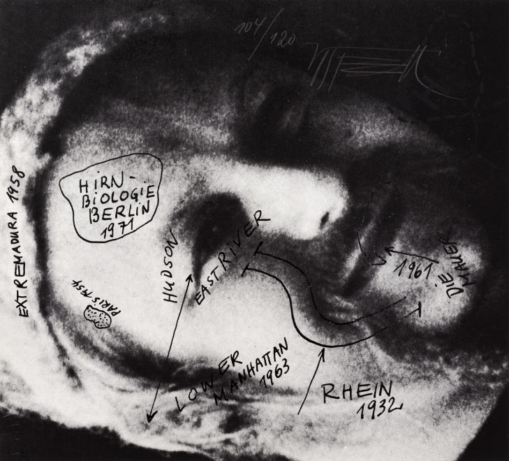 Siebdruck von Wolf Vostell zeigt eine zur Seite gekippte, schwarzweiße Nahaufnahme von Vostells Gesicht. Darüber finden sich in schwarzer Lackfarbe gedruckte, handschriftliche Notizen von Vostell, die biografische Eckdaten und Aufenthaltsorte des Künstlers beinhalten wie RHEIN 1932, LOWER MANHATTAN 1963