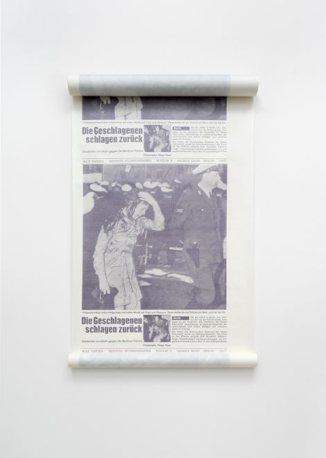 Edition von Wolf Vostell. Papierrolle, auf die als Motiv eine Seite aus dem Stern über die Demonstrationen am 2.6.1967 gegen den Staatsbesuch des iranischen Schahs in Berlin unzählig wiederholt gedruckt wurden. Das Foto zeigt eine blutüberströmte junge Frau, die neben einem Polizisten läuft, im Hintergrund mehr Polizei. Die Überschrift des Artikels: Die Geschlagenen schlagen zurück. Anstelle des Stern-Logos steht die Zeile: WOLF VOSTELL. DEUTSCHE STUDENTENTAPETE. EDITION 8. GALERIE BLOCK BERLIN 1967