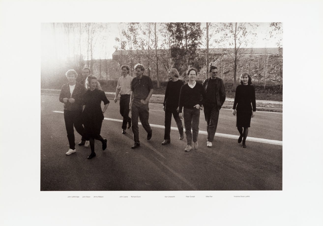 Deckblatt der Grafikmappe Aus Australien mit einem schwarz/weiß Foto der beteiligten Künstler, die über eine Straße laufen. Darunter die Namen der Künstler: John Lethbridge John Nixon Jenny Watson John Loane Richard Dunn Ken Unsworth Peter Tyndall Mike Parr Vivienne Shark LeWitt