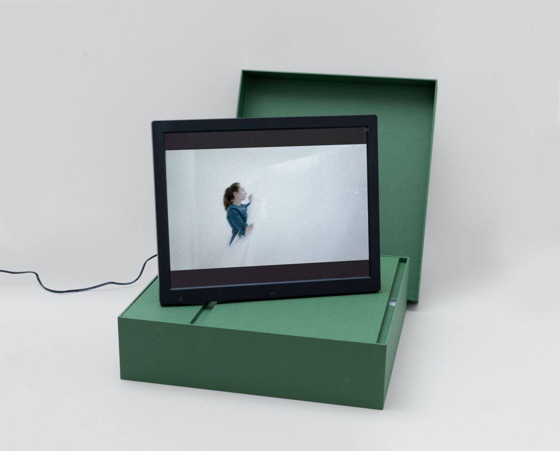 The edition ATEM by the artist Mehtap Baydu. A digital picture frame, on which a video of the performance is shown, stands on the green linen case made for it