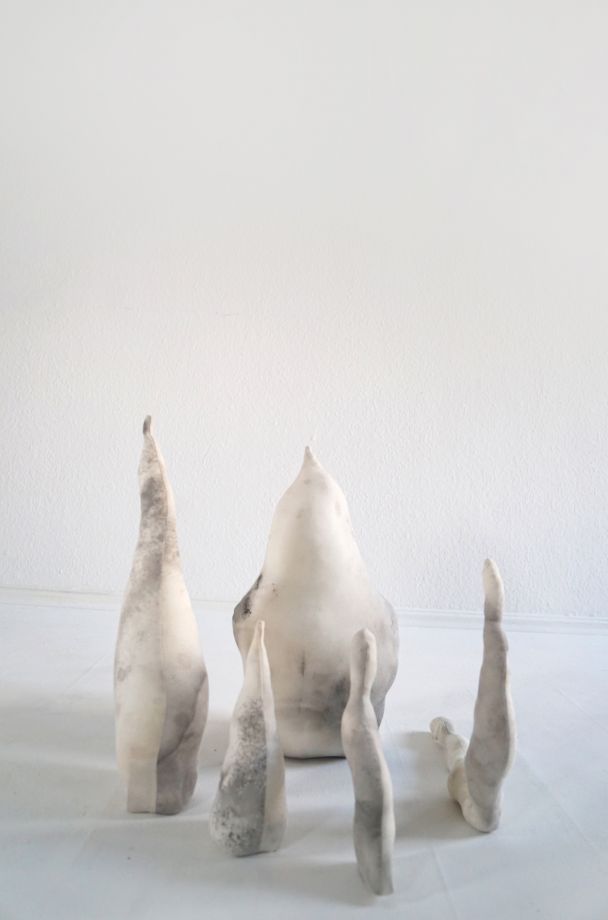 Multi-part sculptural installation by Dorothee Diebold with light, organically shaped objects and grey tonal variations, arranged loosely on a pale floor in front of a white wall.