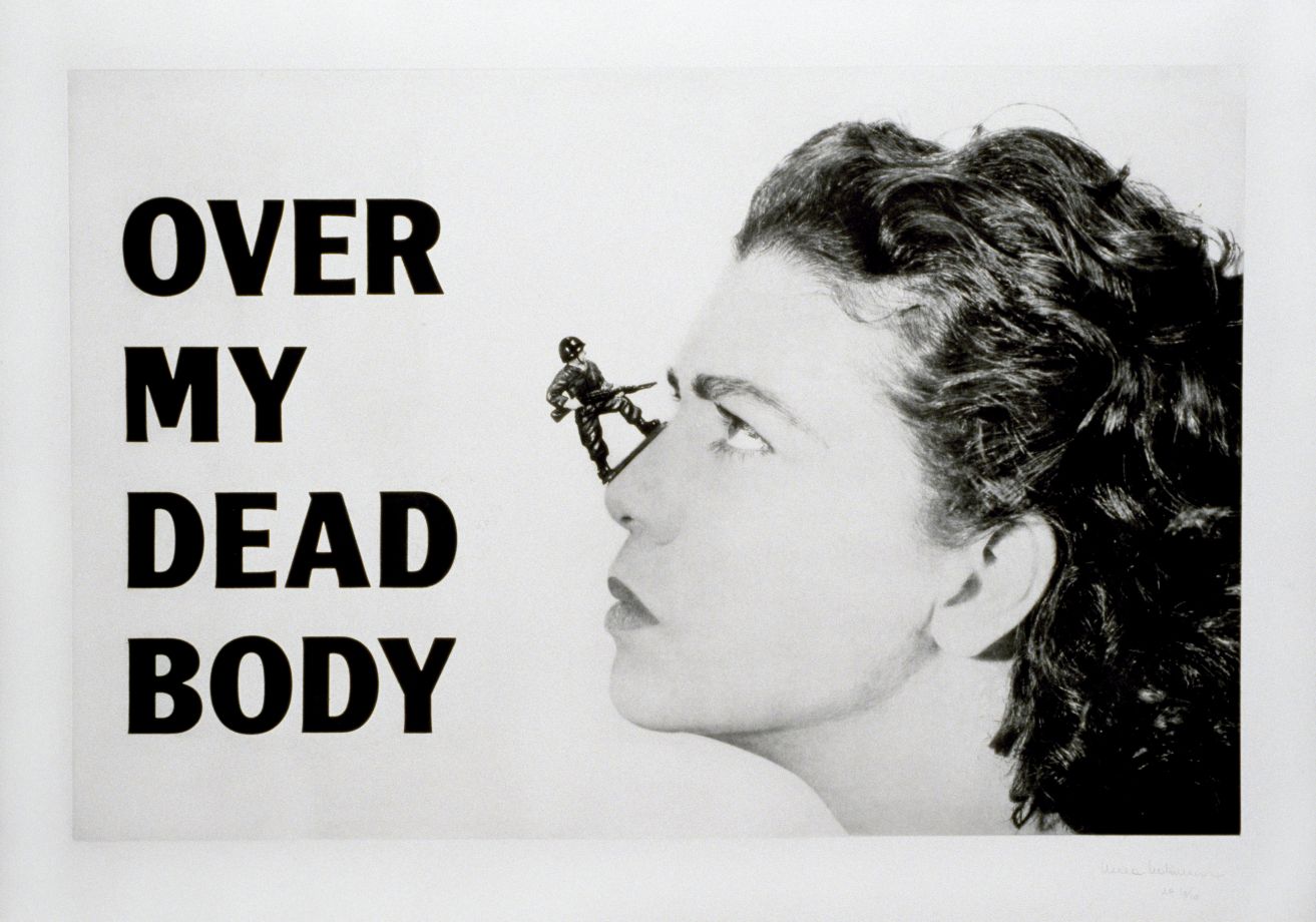 Druck von Mona Hatoum. Ein schwarz-weiß Portrait von Mona Hatoums Kopf. Auf ihrer Nase steht ein kleiner Spielzeugsoldat mit einem Gewehr in den Händen, das er auf sie richtet. Auf der linken Bildseite steht in fett schwarz OVER MY DEAD BODY